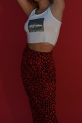 A model wearing a white crop top with a black car graphic and red high-waisted leggings with a black abstract pattern, set against a solid red background.