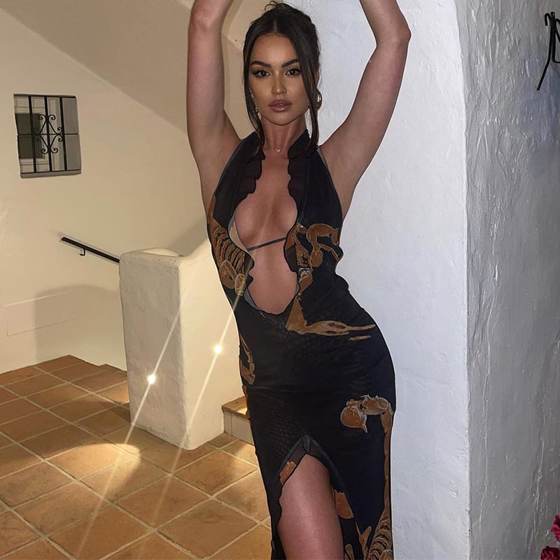Woman in a black dress with gold patterns posing indoors.