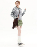 Person wearing a striped sweater, green shorts, and white socks with black shoes on a white background