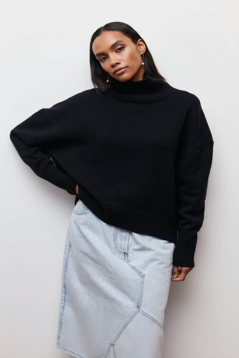 Person wearing a black turtleneck sweater and light blue jeans on a plain background