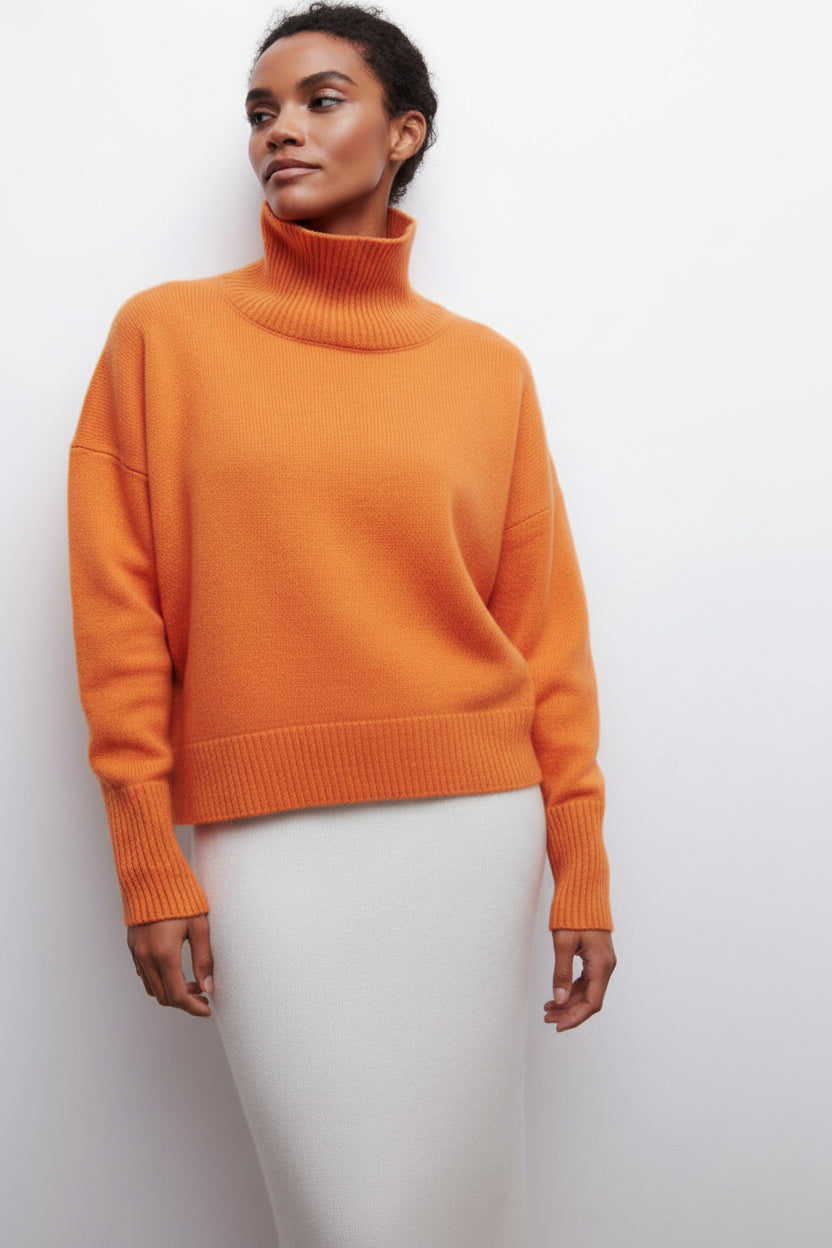 woman wearing an orange sweater and white pants against a light gray background