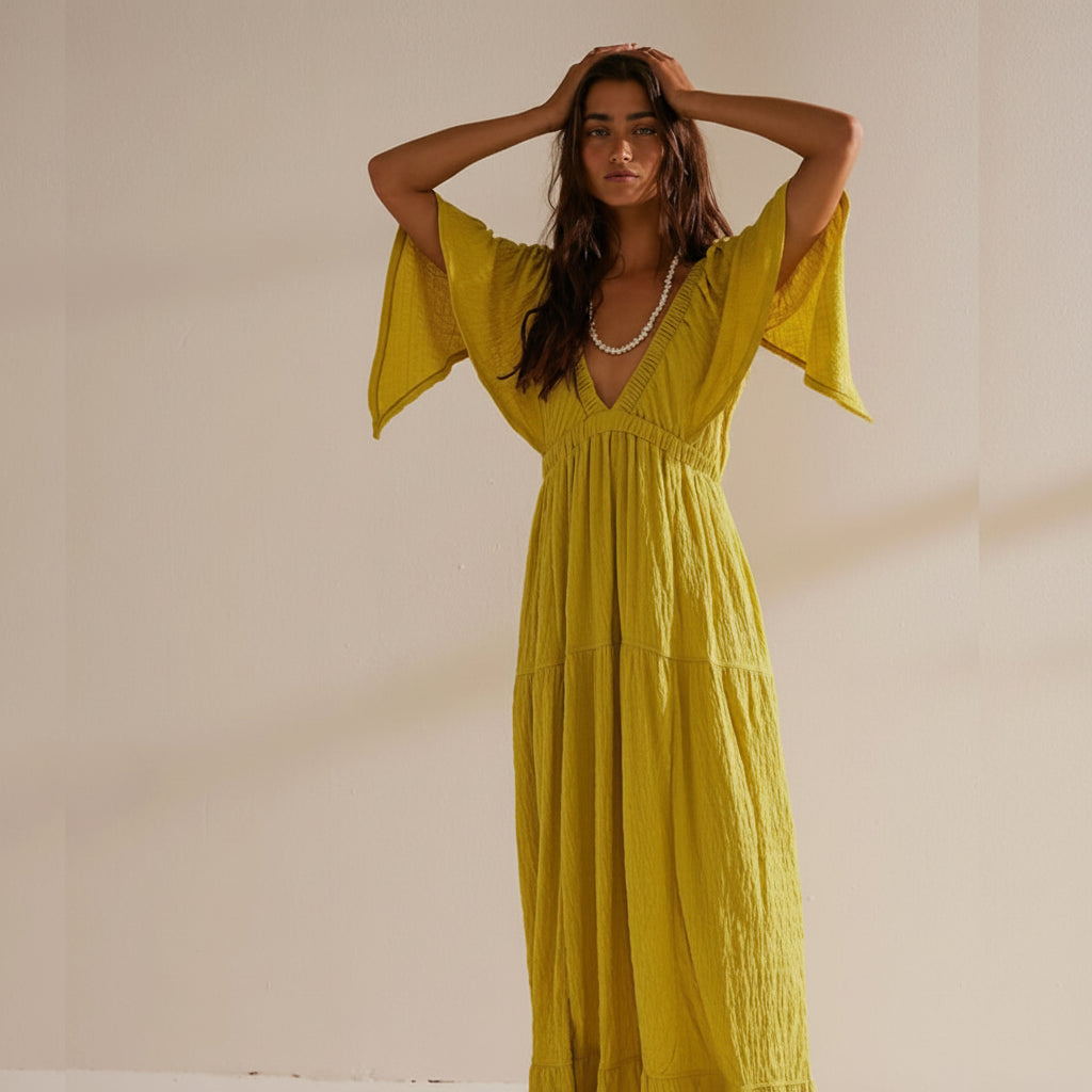 Woman wearing a yellow dress with wide sleeves against a neutral background