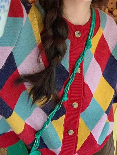 Person wearing a colorful patterned cardigan with a braided hair and green strap over shoulder.